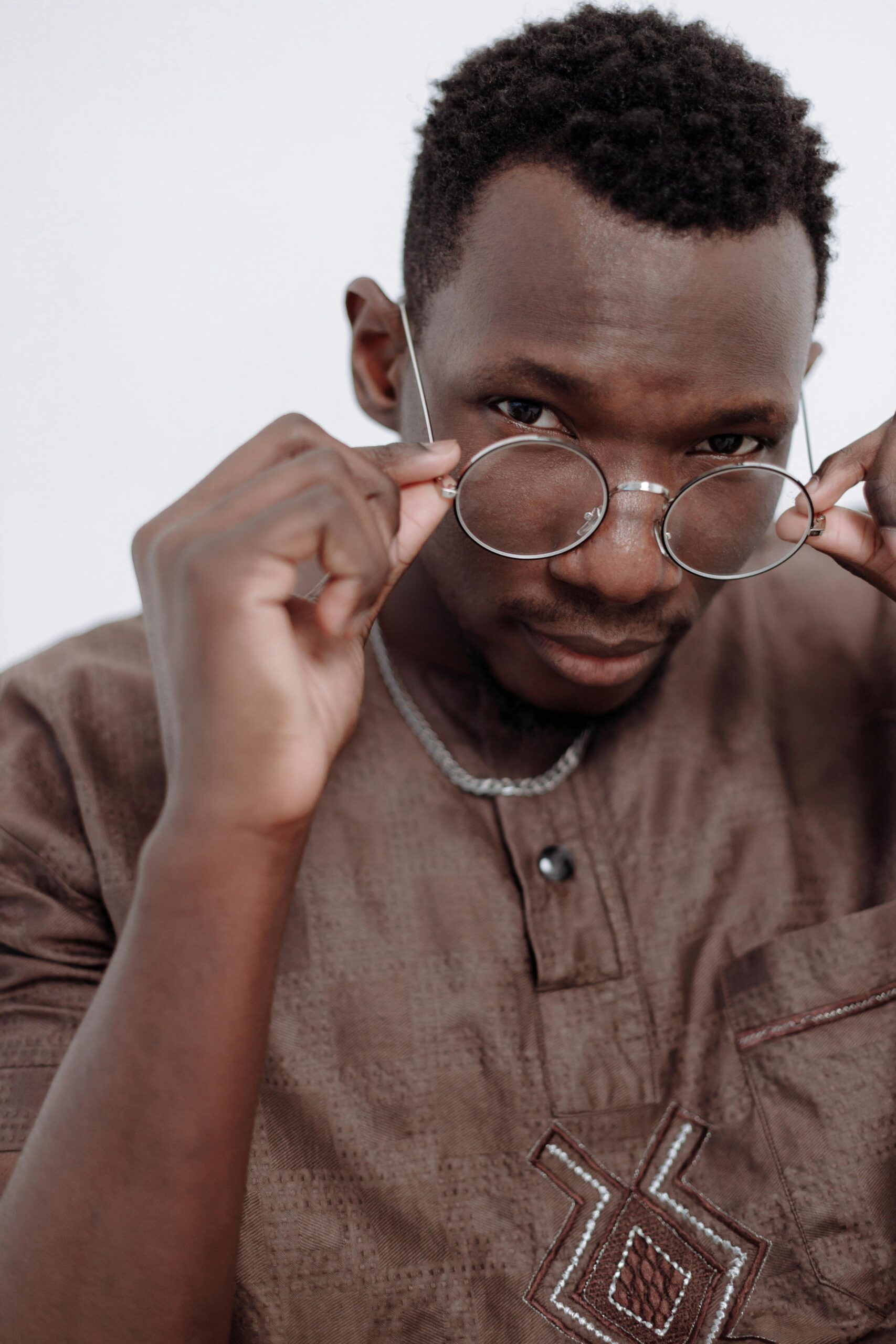 Close-up portrait of a young man adjusting his eyeglasses, wearing a brown traditional shirt.